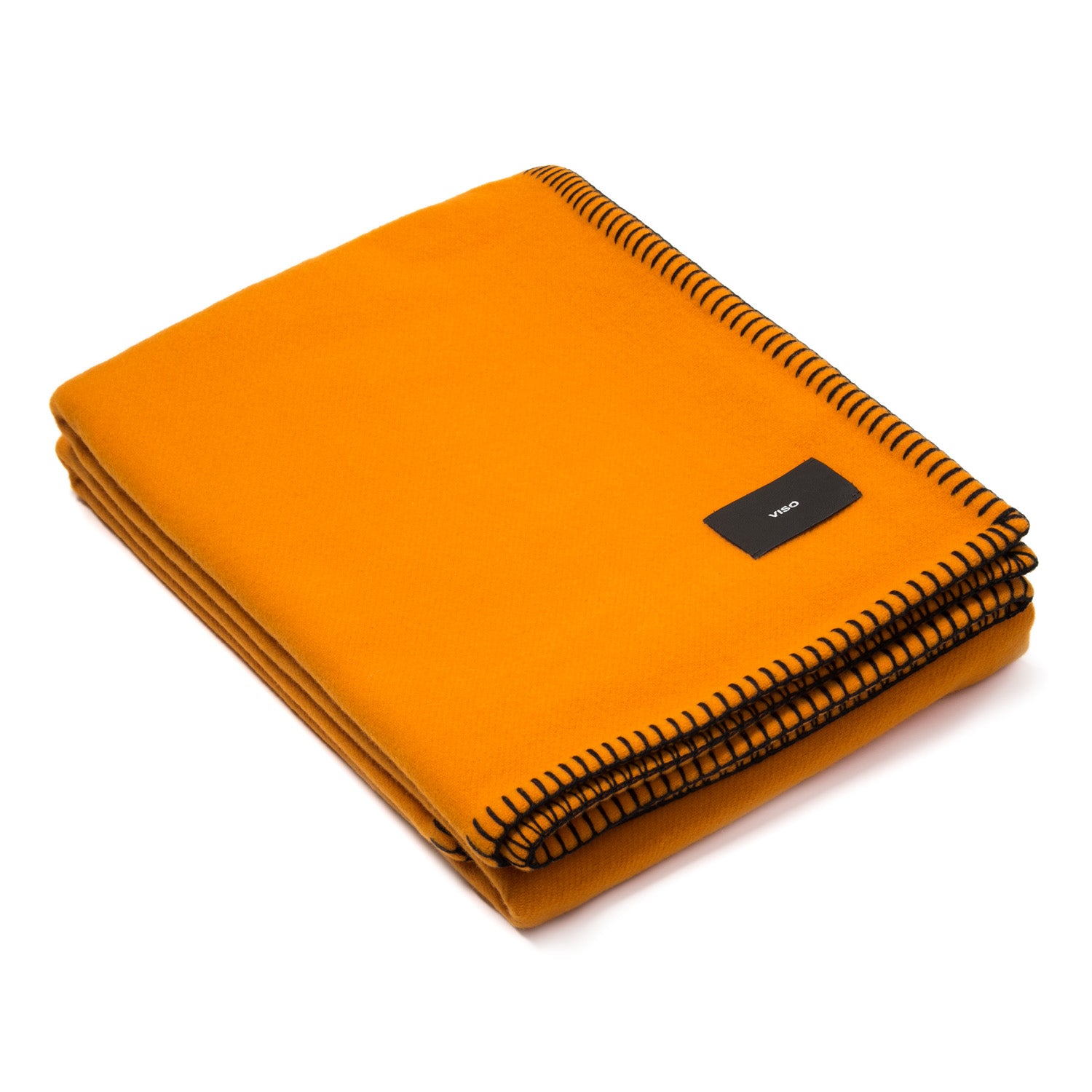 A folded orange Merino wool blanket with black contrast stitching and a tag visible on the lower side.