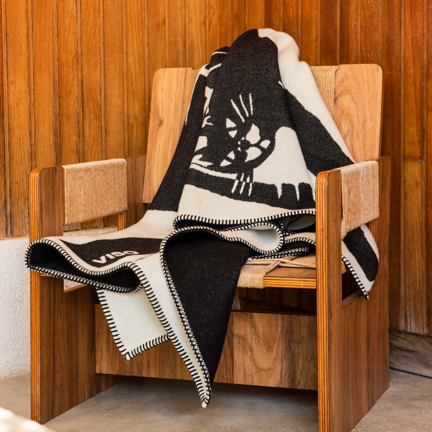 A merino blanket featuring a black-and-white cat design on a wooden armchair in a living room.
