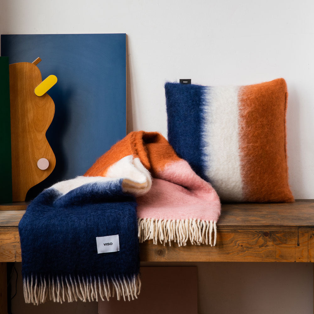 An orange, white and blue striped blanket and pillow on a shelf.