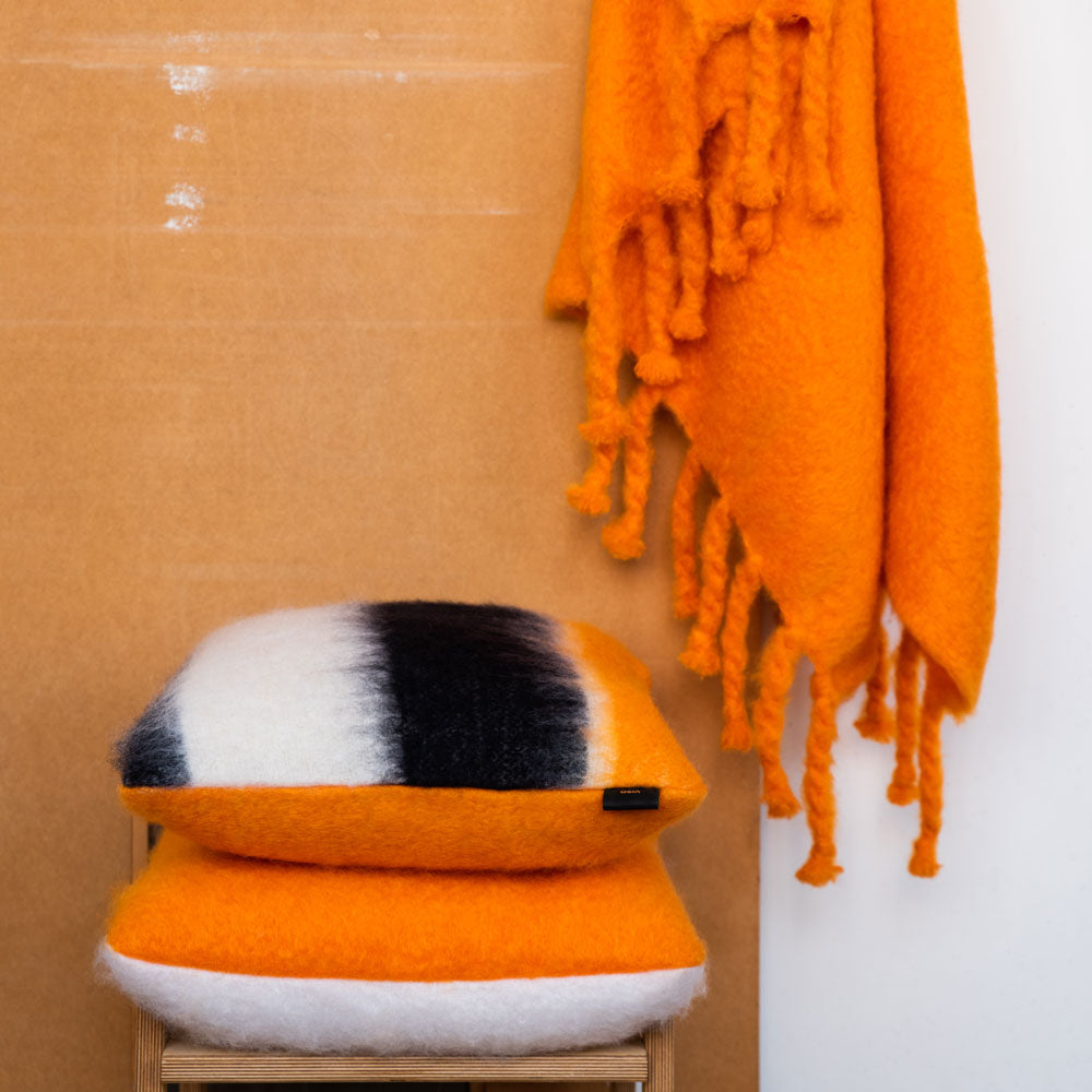 An orange and white mohair pillow on a wooden chair and an orange mohair blanket draped over it.