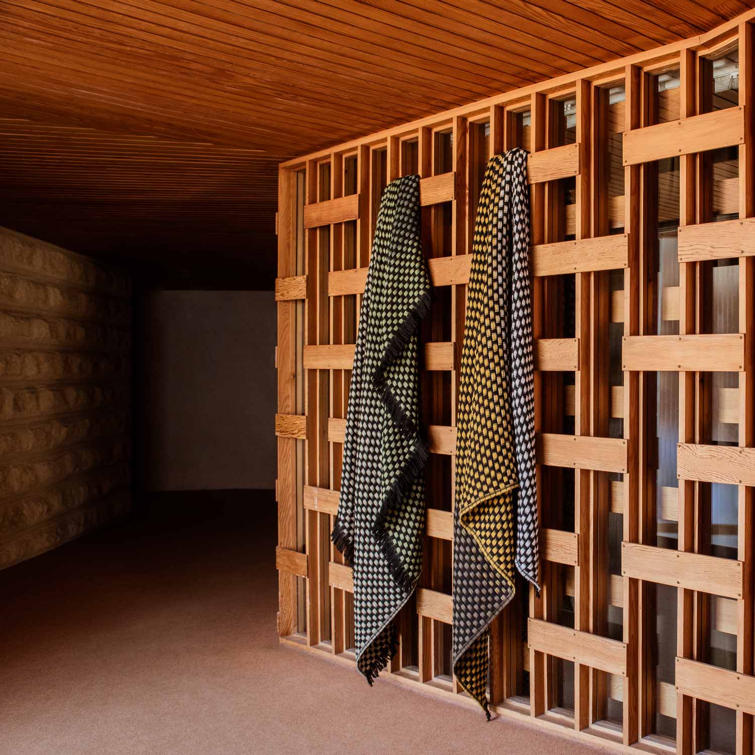 Two basketweave-patterned blankets – one green and one yellow – are draped over a wooden wall.
