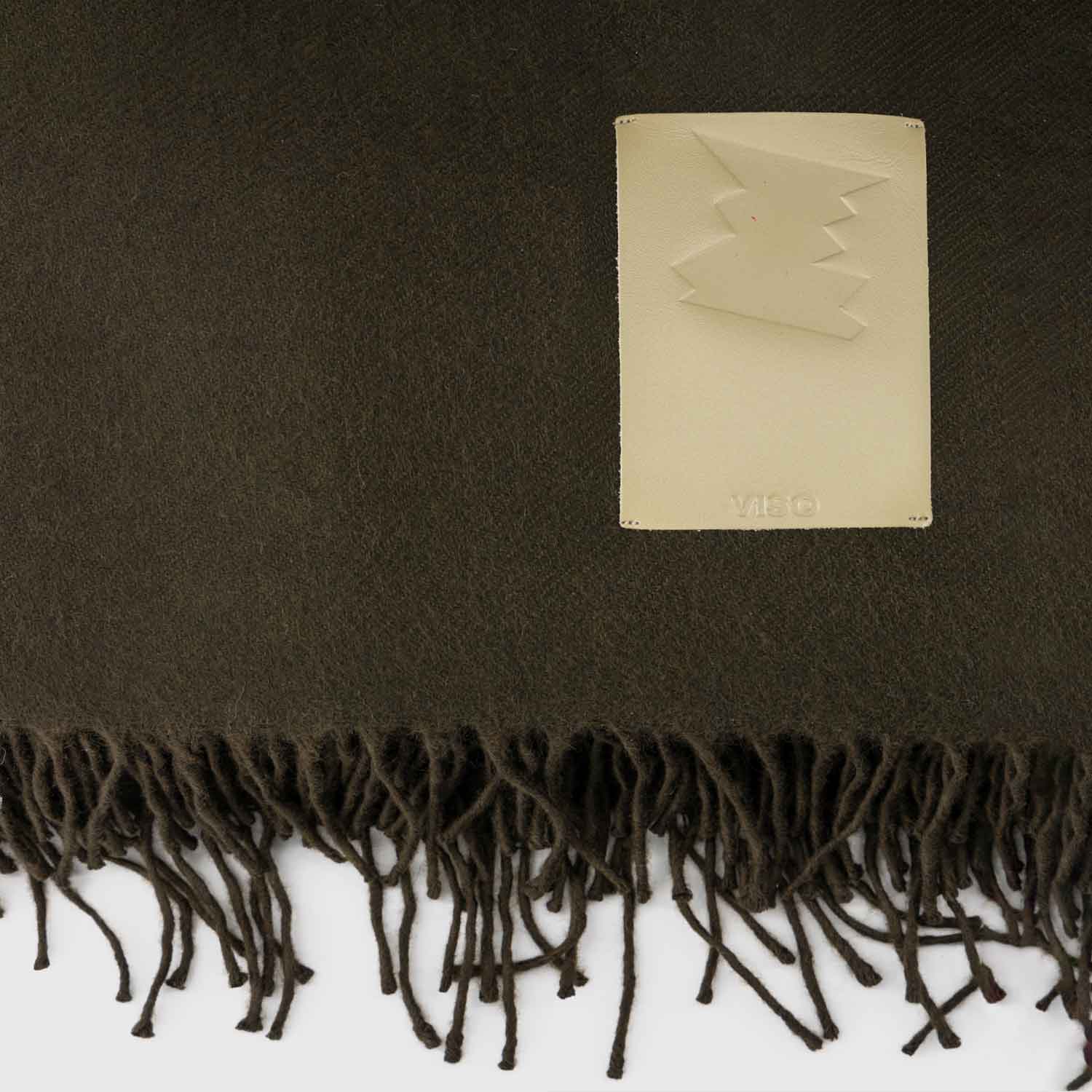 Close-up of the cream leather label on a dark green fringed cashmere blanket