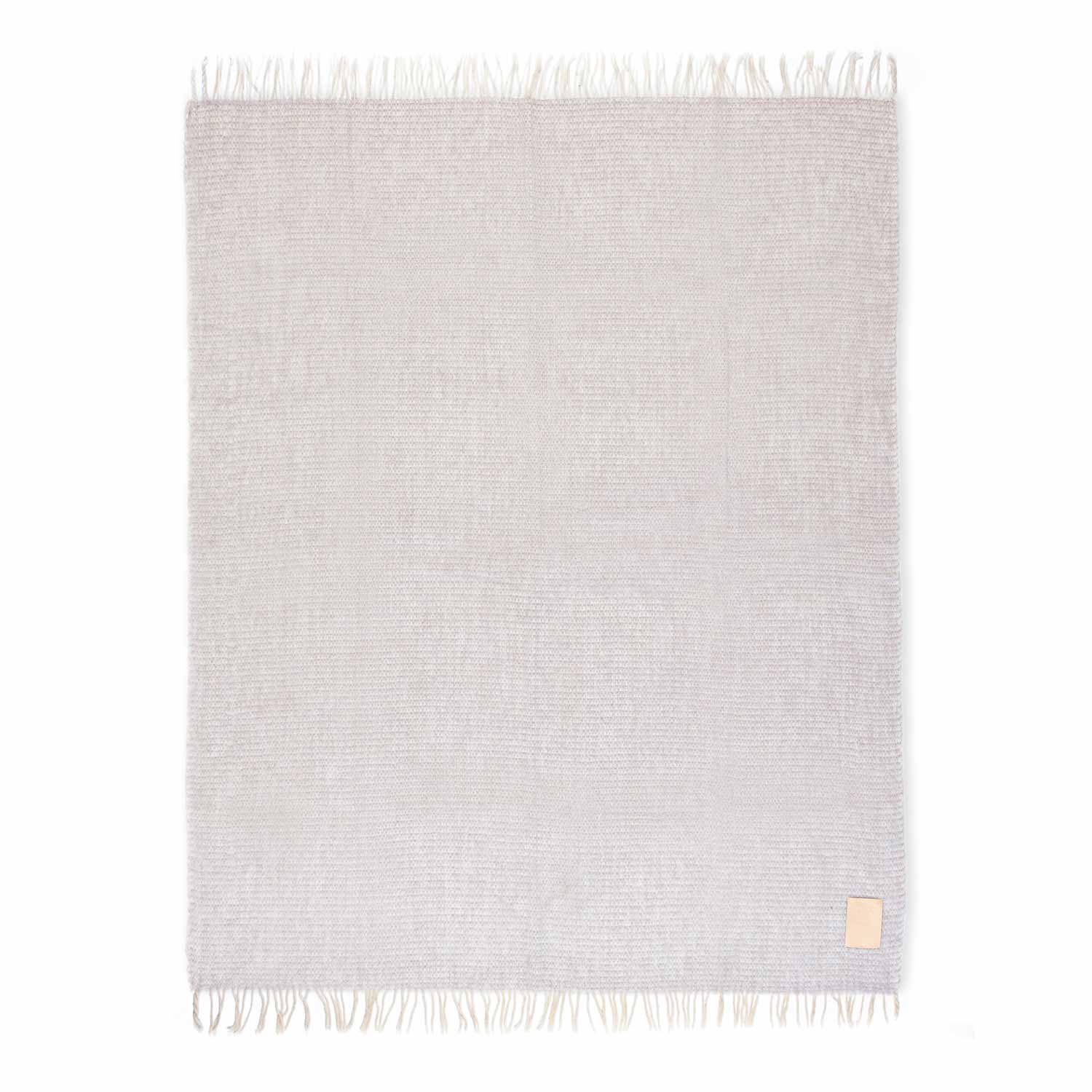 A cream and beige colored mohair blanket with fringe, displayed neatly folded with a tag visible on one corner.