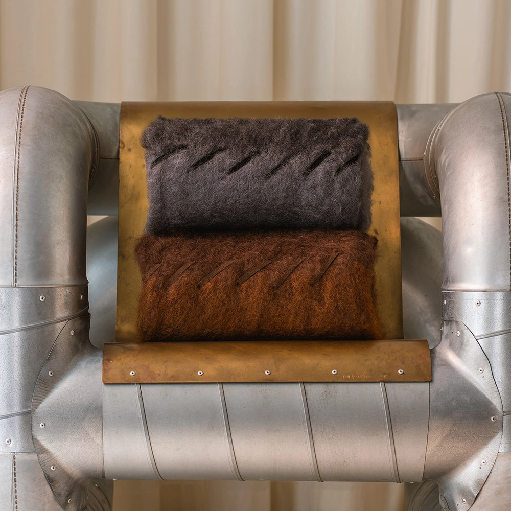Metallic chair with a wooden shelf holding two folded mohair blankets, one gray and one brown.