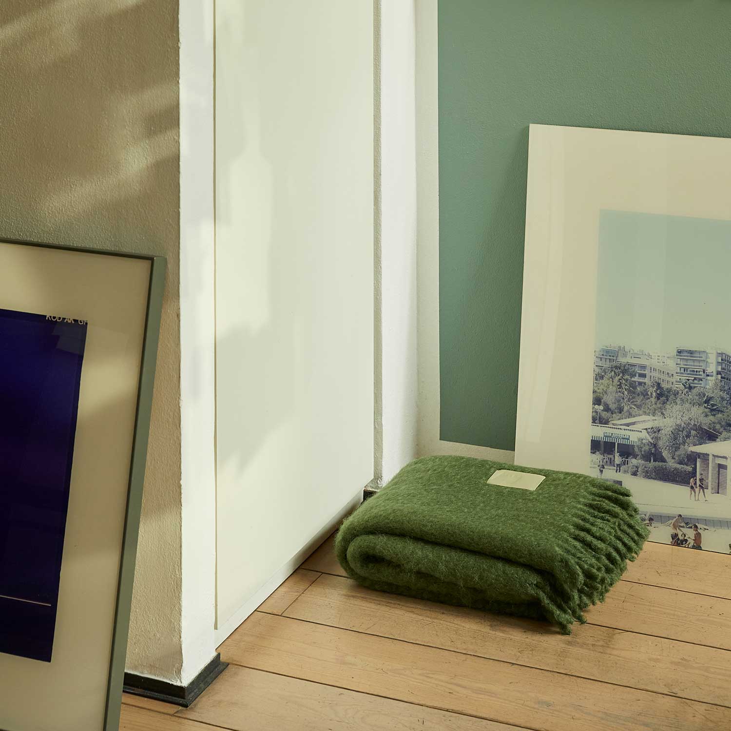 Inside a room, there is a green mohair blanket folded on the floor.
