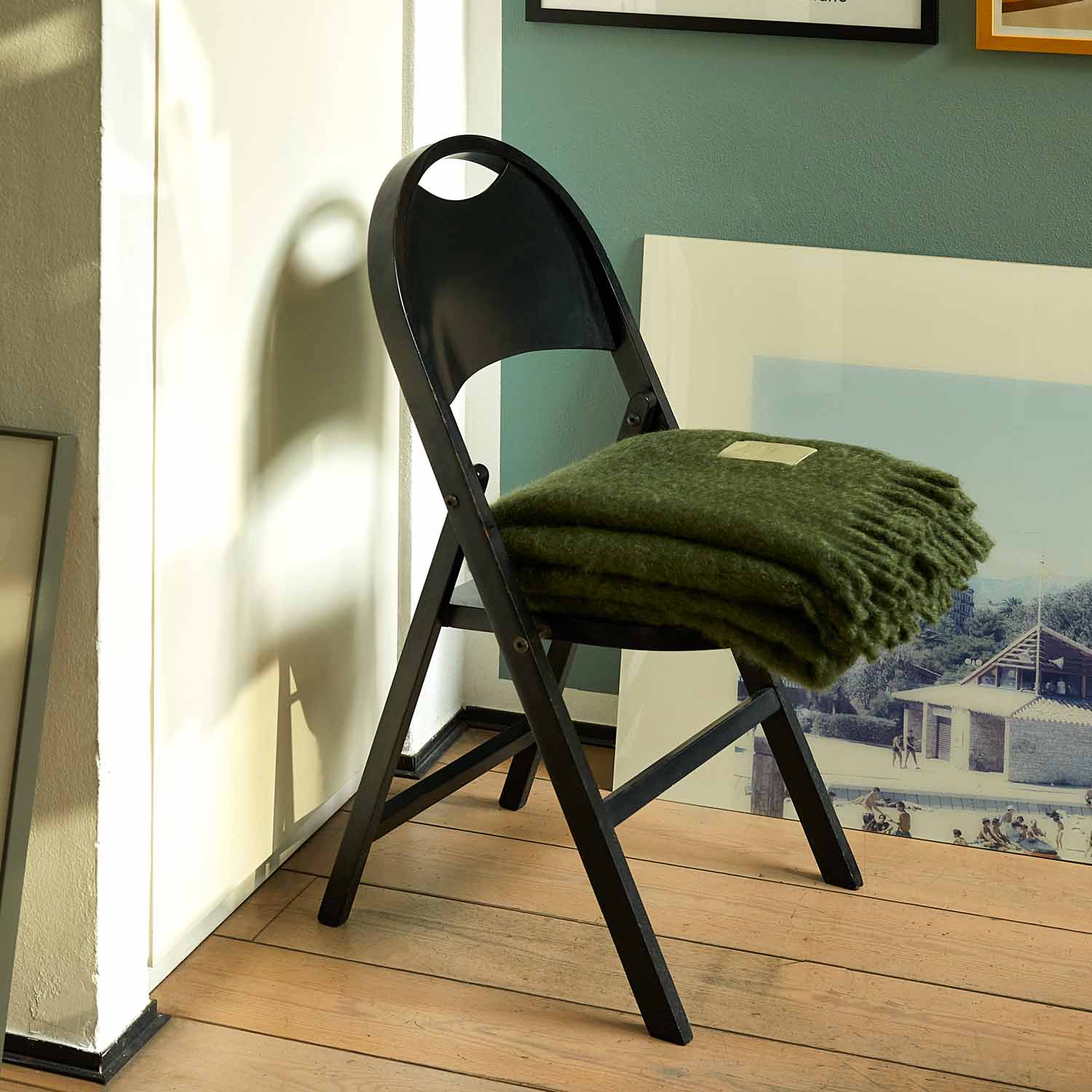 In a room, there is a black chair with a green mohair blanket folded over it.