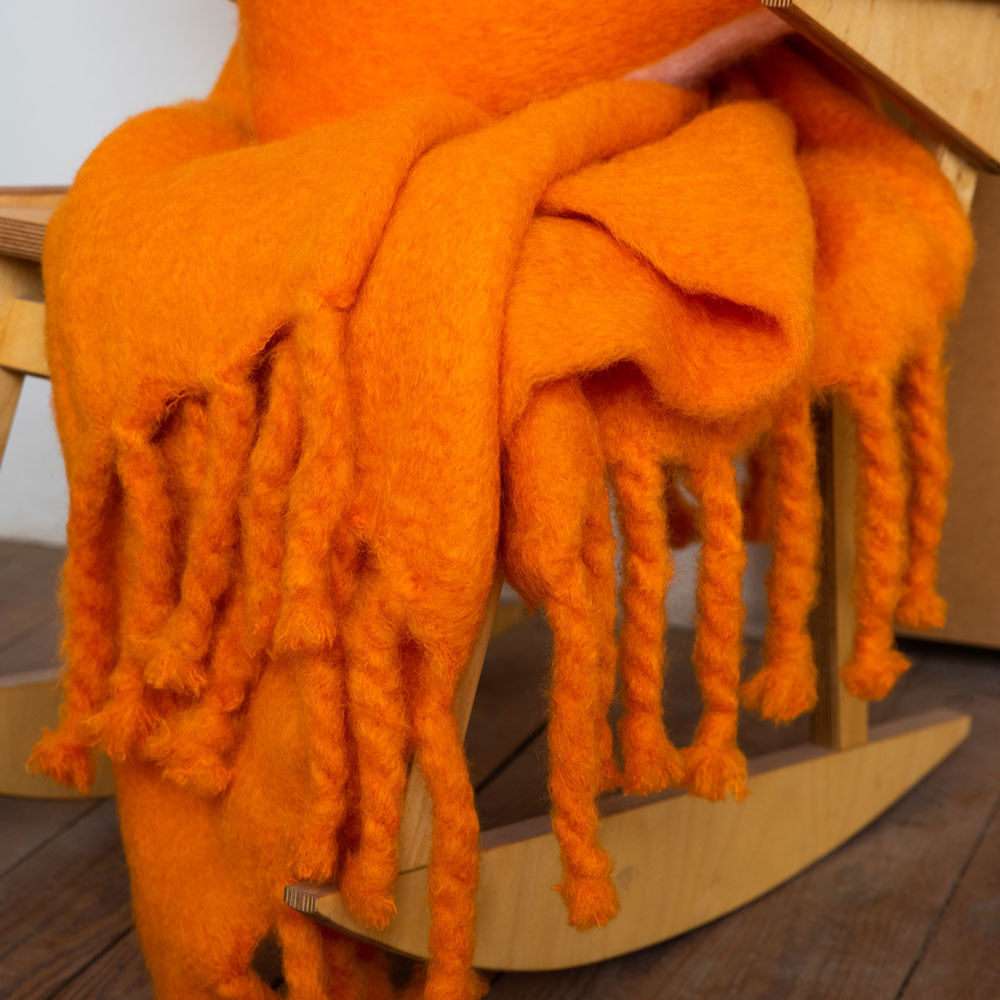 An orange mohair blanket draped over a wooden rocking chair.