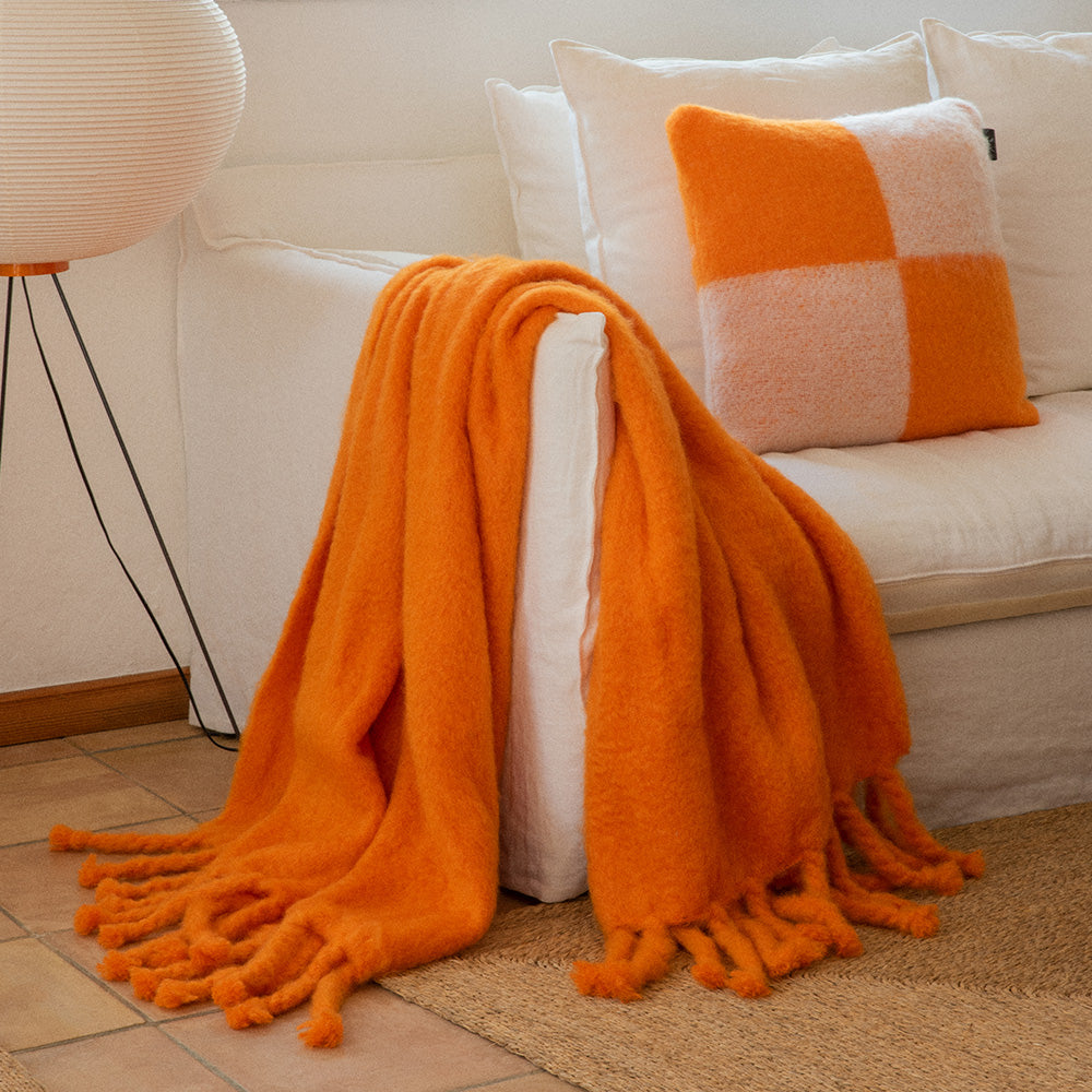 An orange mohair blanket draped over a white linen sofa and an orange checked mohair pillow.