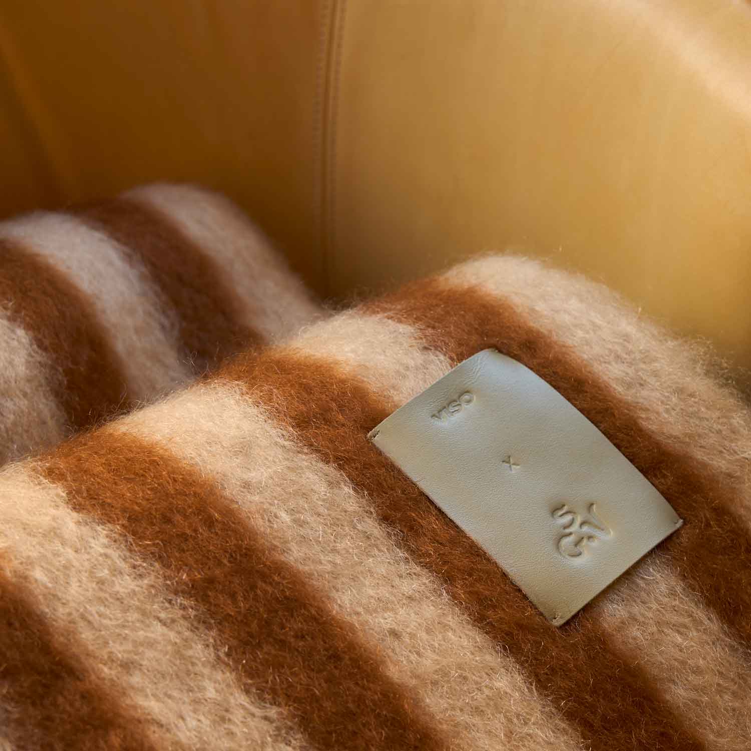 A close-up of the texture of a mohair blanket featuring brown and beige stripes, with a leather label.