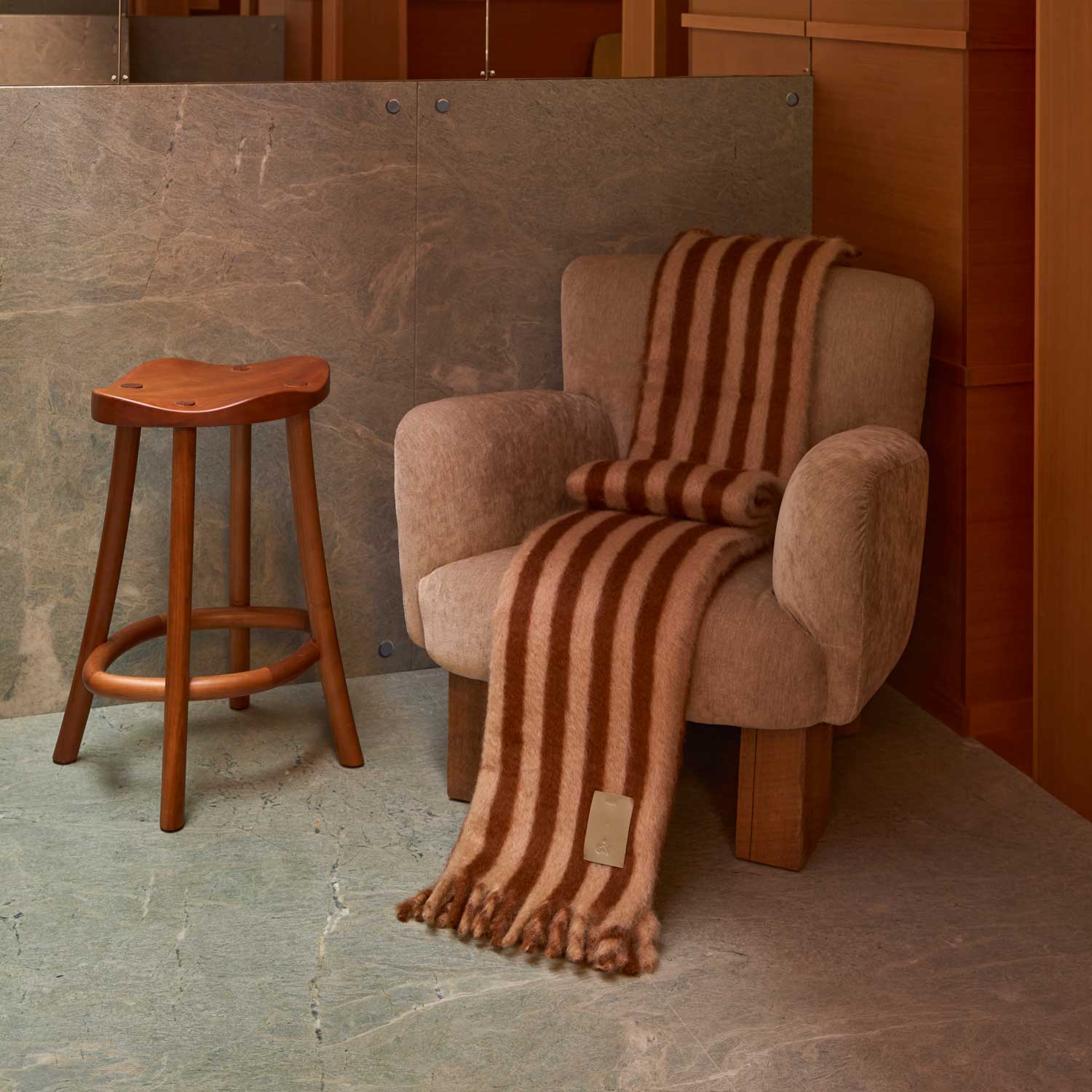 A small corner of an elegant, cosy living room with a chair and an armchair, draped with a beige and brown striped mohair blanket.