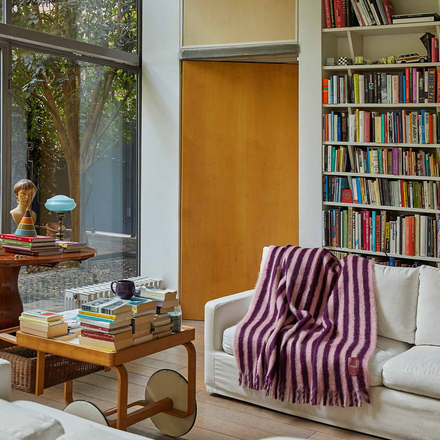 A living room with a bookcase and a sofa, featuring a purple and pink striped mohair blanket.