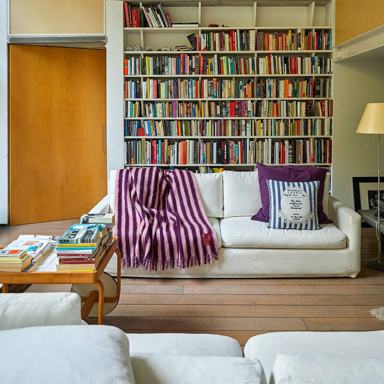 A living room with a bookcase and a sofa, featuring a purple and pink striped mohair blanket.