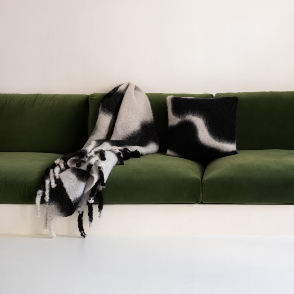 A black-and-white tie-dye mohair blanket and pillow on a green sofa.