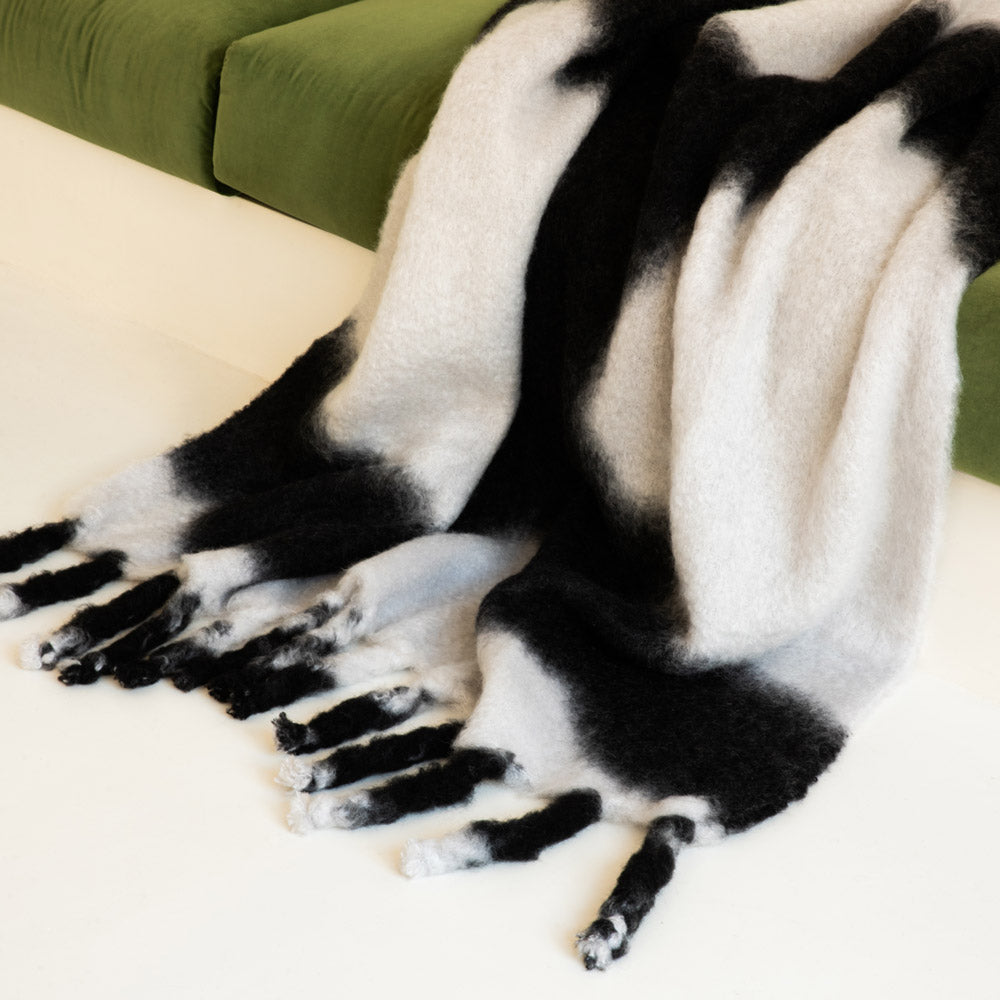 A black-and-white tie-dye mohair blanket on a green sofa.