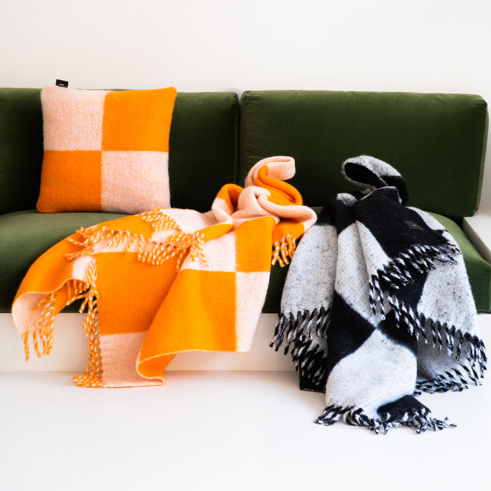 Mohair blankets and pillow in a black-and-white and orange checkered pattern, on a green sofa.