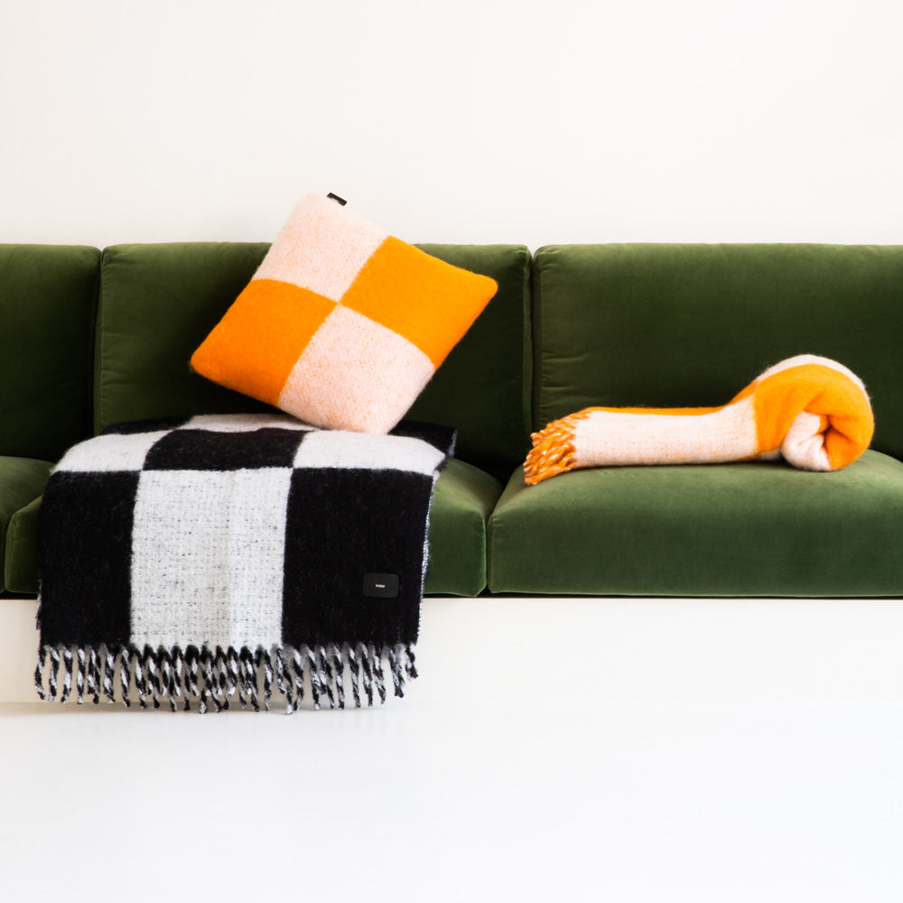 Mohair blankets and pillow in a black-and-white and orange checkered pattern, on a green sofa.