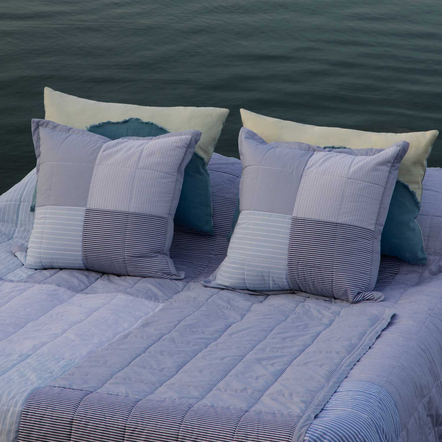 Bed with patterned pillows and quilt against a body of water
