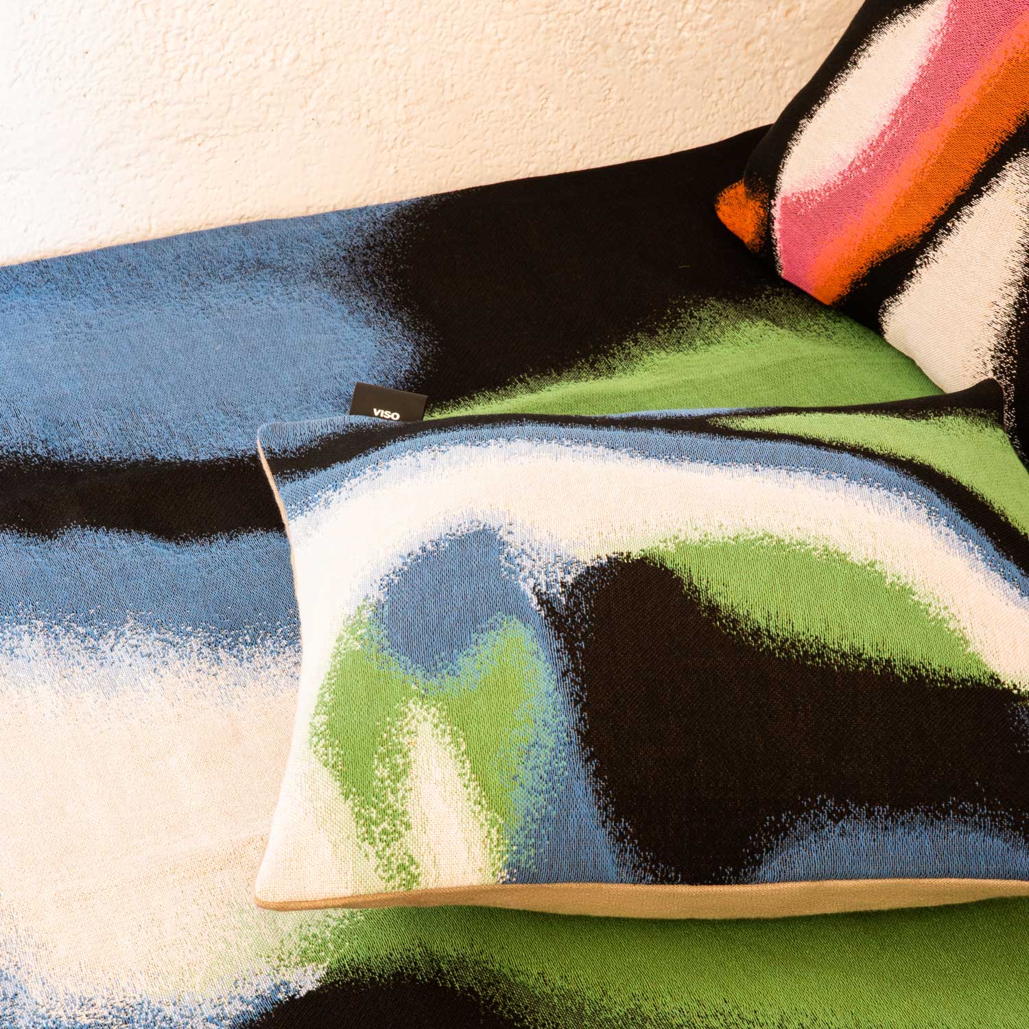 A close-up of a bed with blanket and tapestry pillows featuring an abstract design in bright colors.