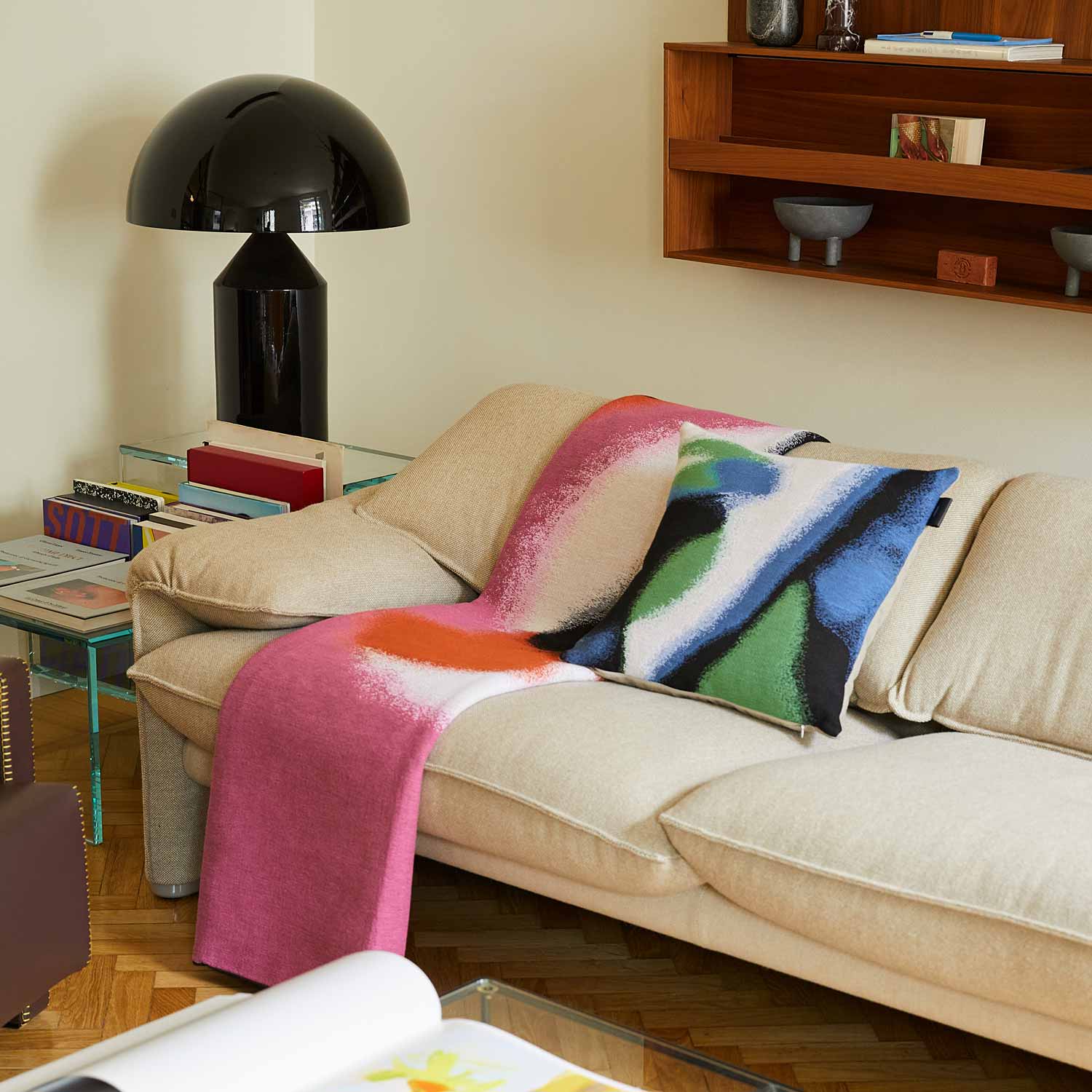 A fully furnished living room with a white sofa, complete with blankets and tapestry pillows featuring a brightly colored abstract design set against various decorative elements