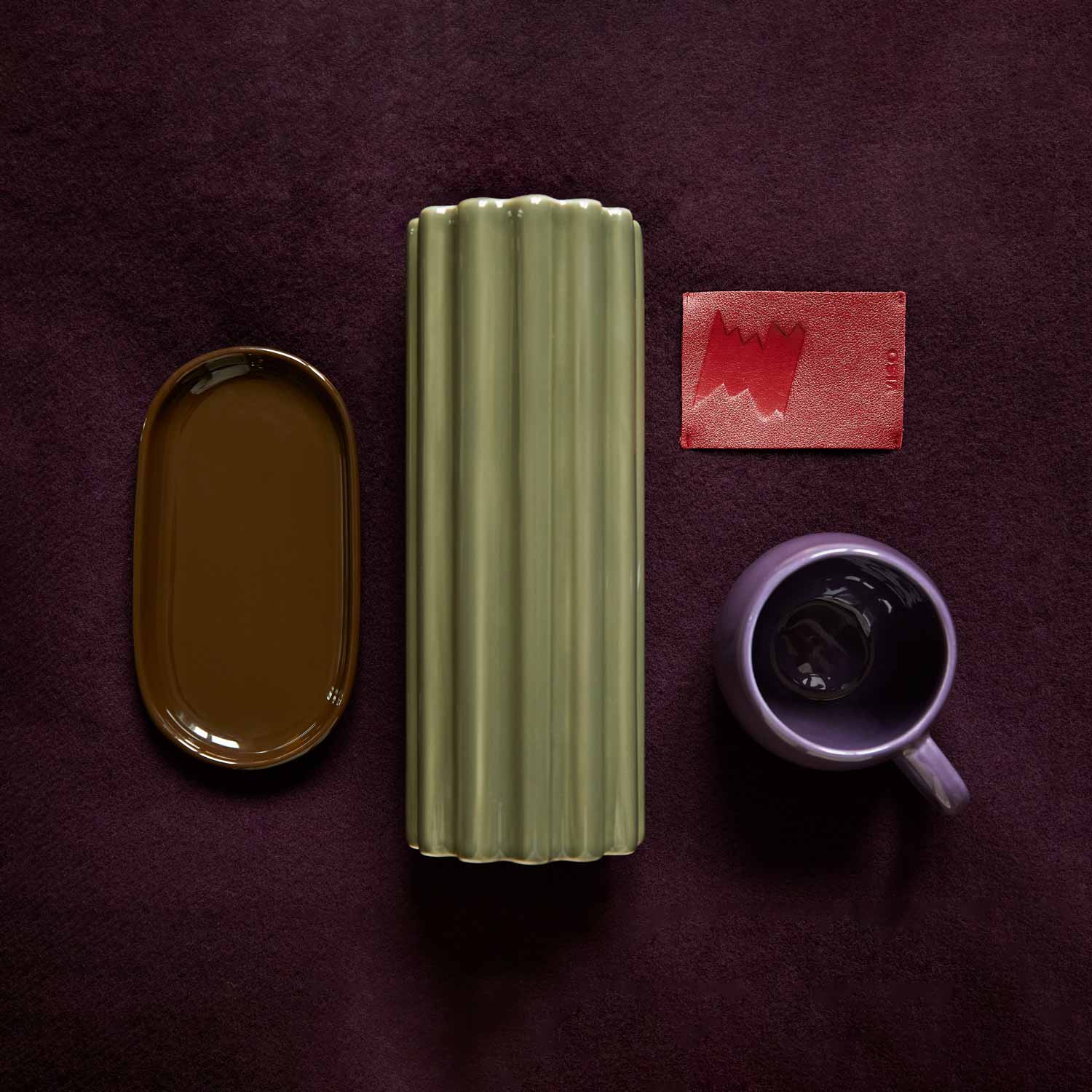 An arrangement of various porcelain pieces in green, purple and brown, set against a purple merino blanket.