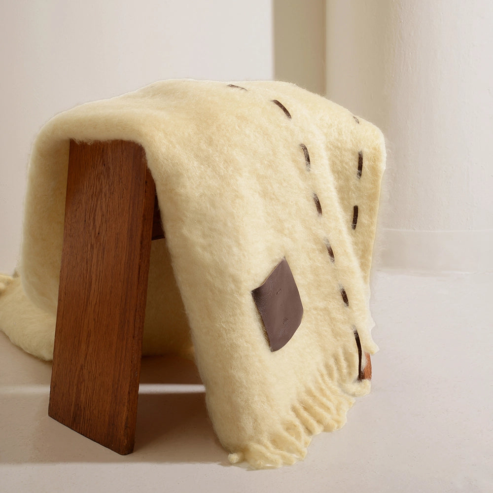 Wooden stool with a cream-colored blanket draped over it on a light background