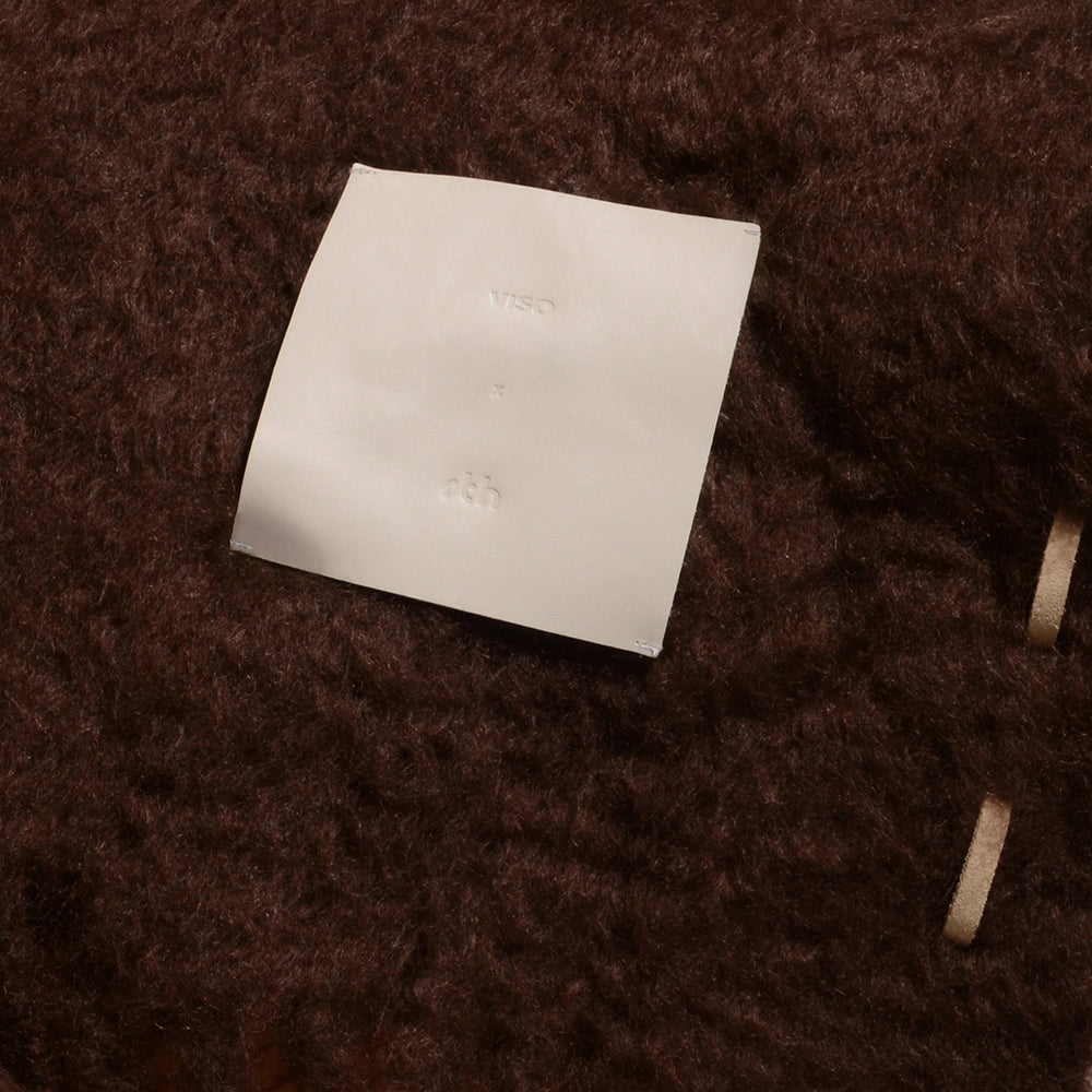 Cream square leather label with brand logos on a chocolate mohair  textured surface – Ready to Hang X Viso Project