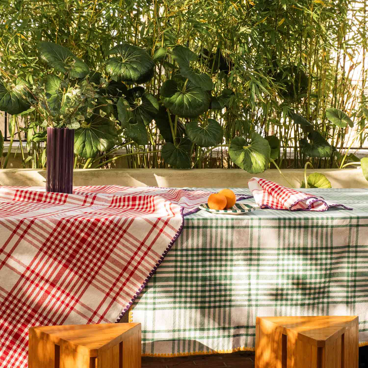 A table in a Mediterranean country house, laid with red, purple, yellow and green tablecloths, with napkins in the same colors, and ceramic crockery and a vase on top.