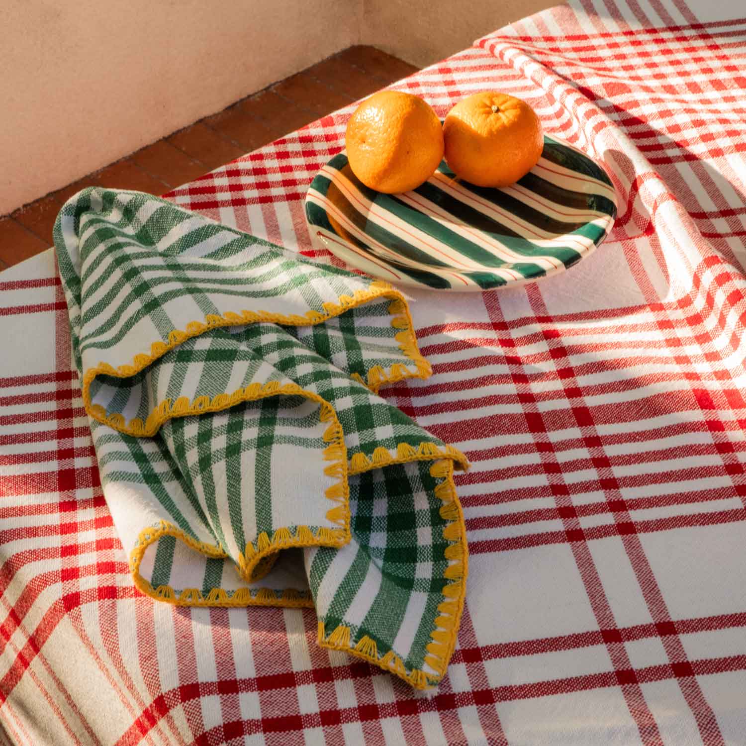 A red chequered tablecloth next to a green-striped ceramic plate and a green and yellow chequered napkin.