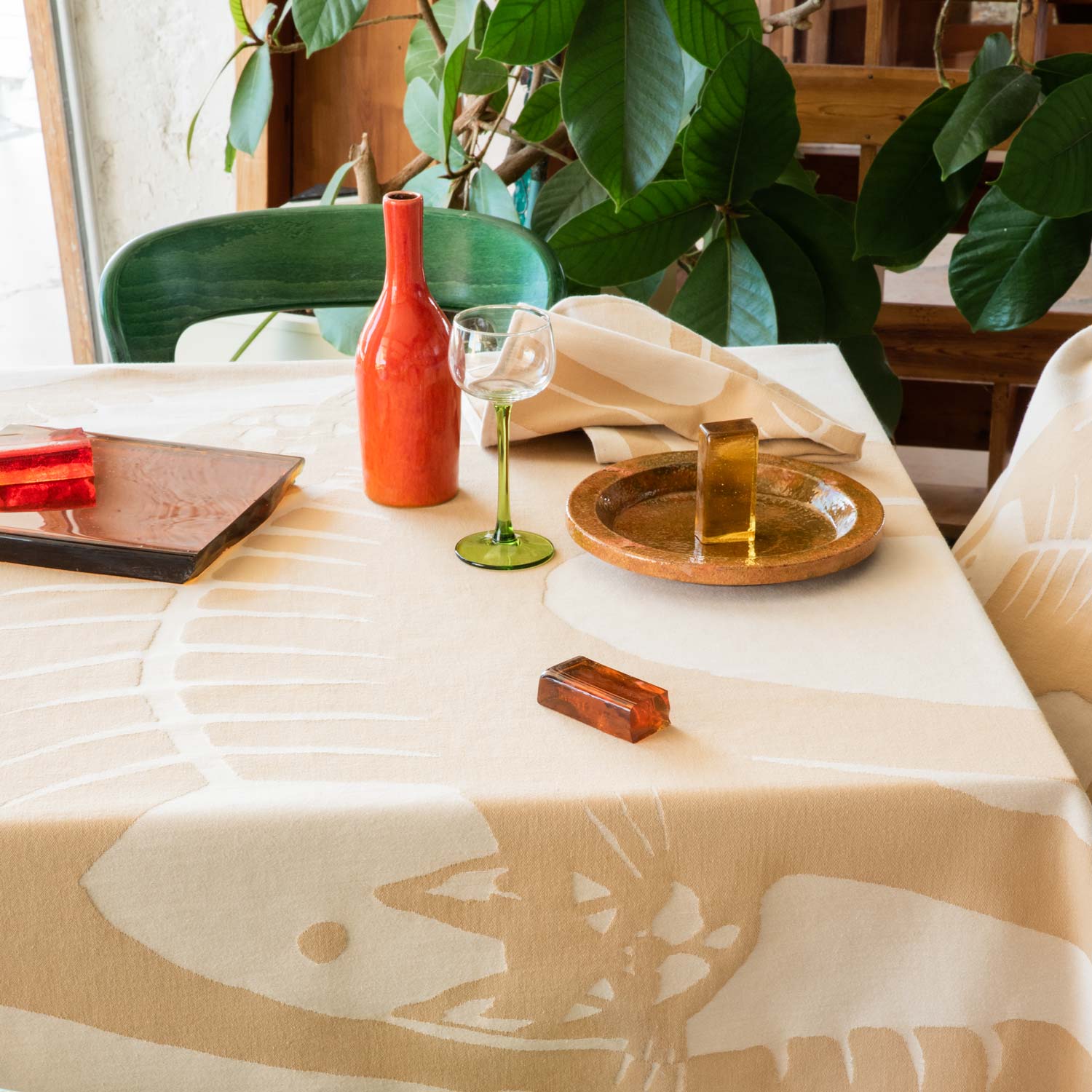 A table set for a meal, with a beige and cream napkin and tablecloth and a matching pillow on the chair featuring an illustration of some cats.