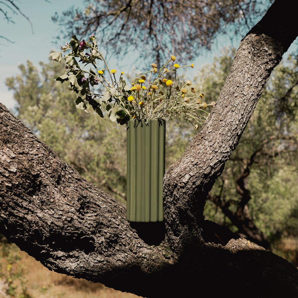 Green vase with flowers hanging from a tree branch