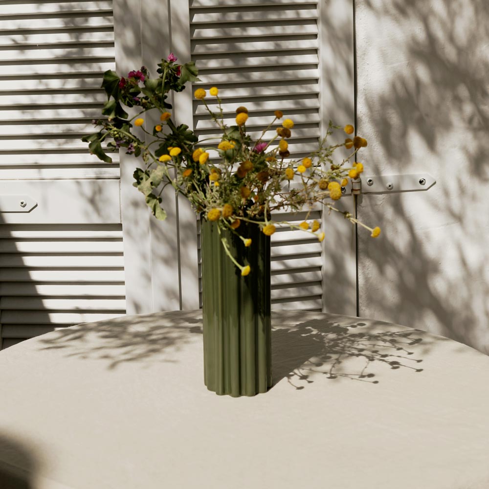 Green vase with yellow flowers against a neutral background