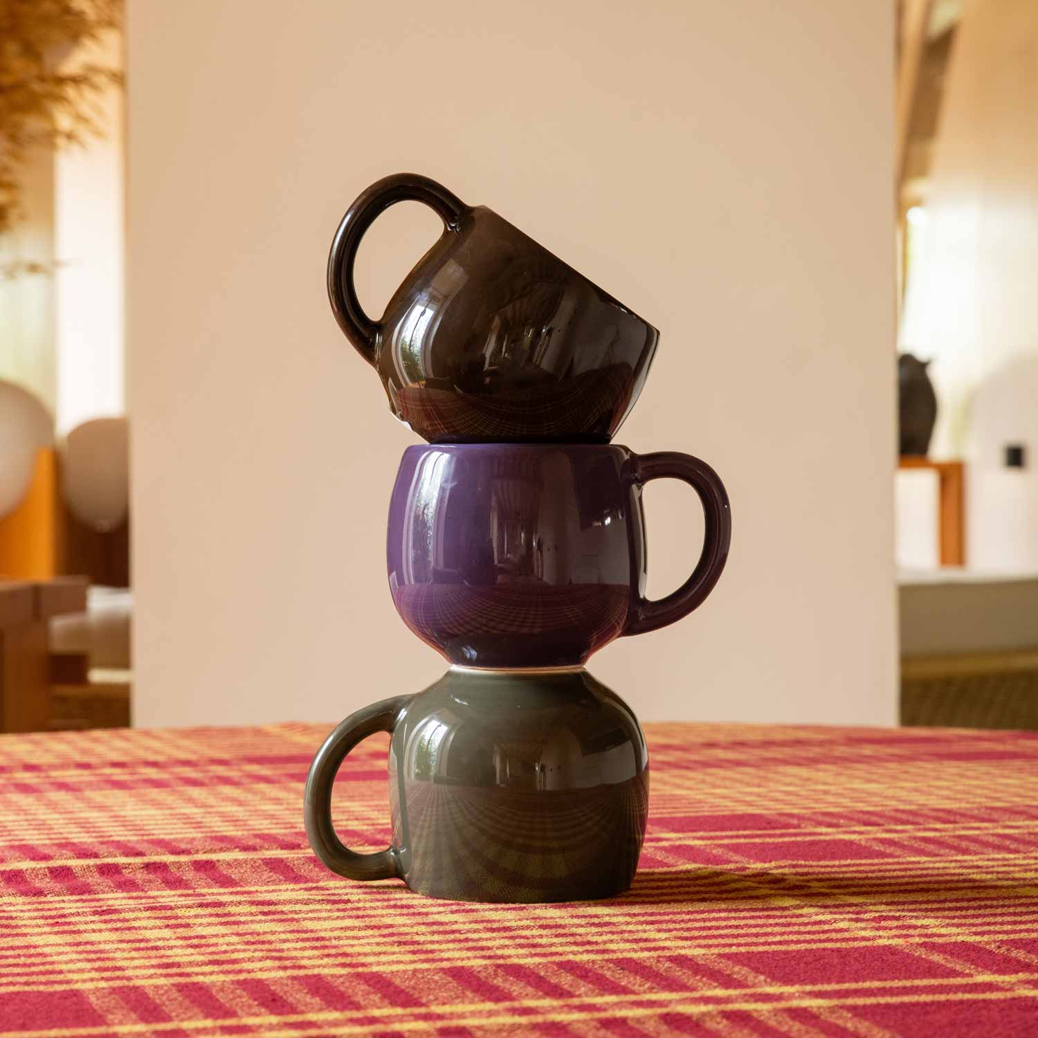 Three ceramic mugs in shades of green, brown and purple, stacked on top of one another on a table.