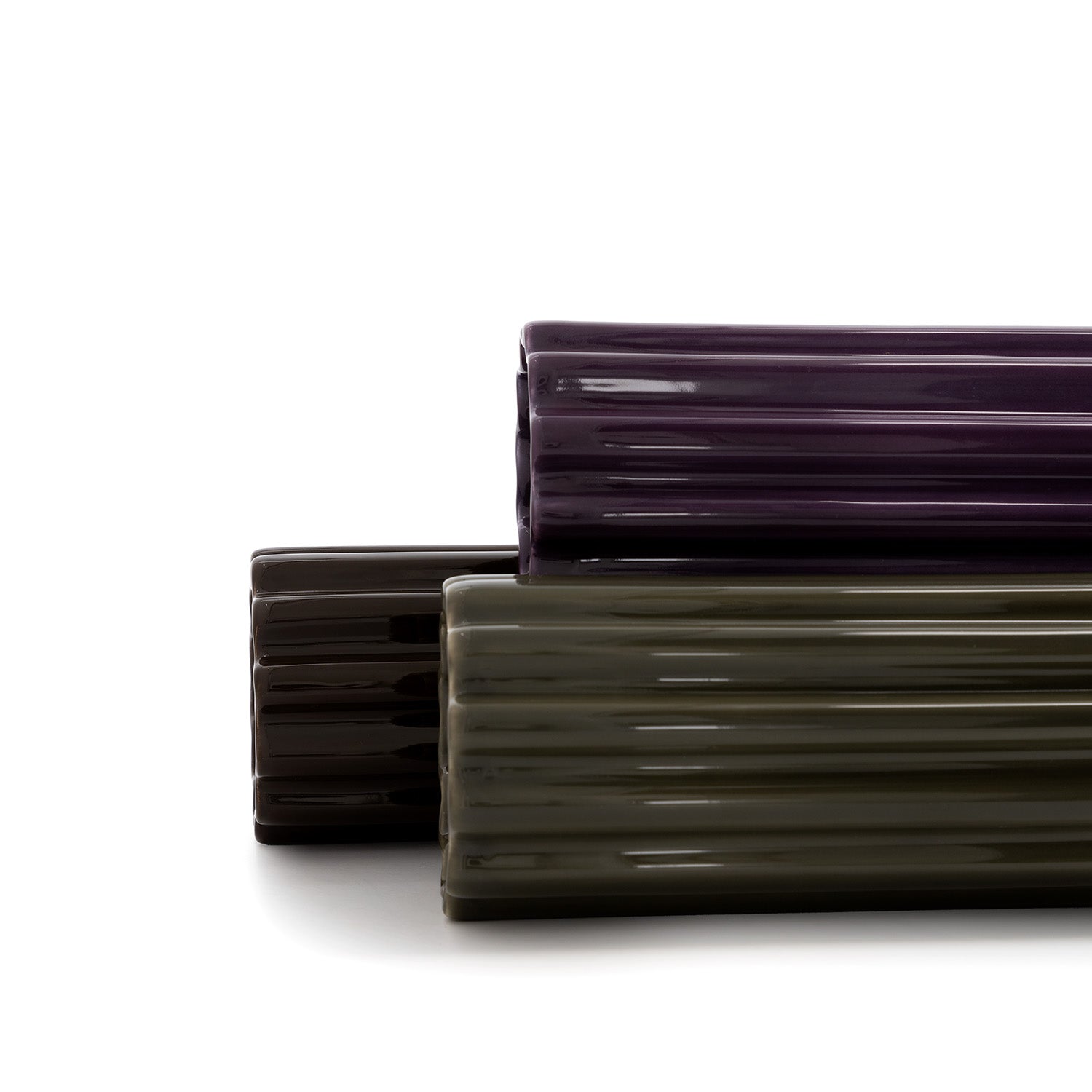 Three high-gloss ceramic vase in purple, green and brown,  with a ribbed design, standing against a white background.
