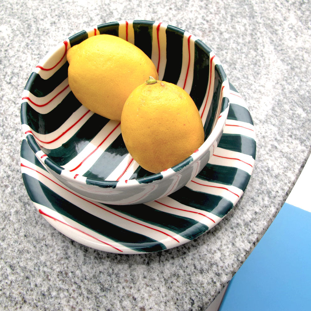 A plate and bowl with a design featuring white, green and red stripes on the dining table.
