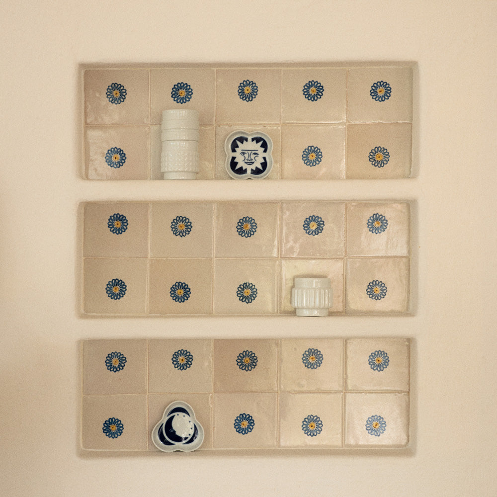A built-in shelf on a white Mediterranean-style wall with colourful tiles. On top of these are white and navy cups and trays.
