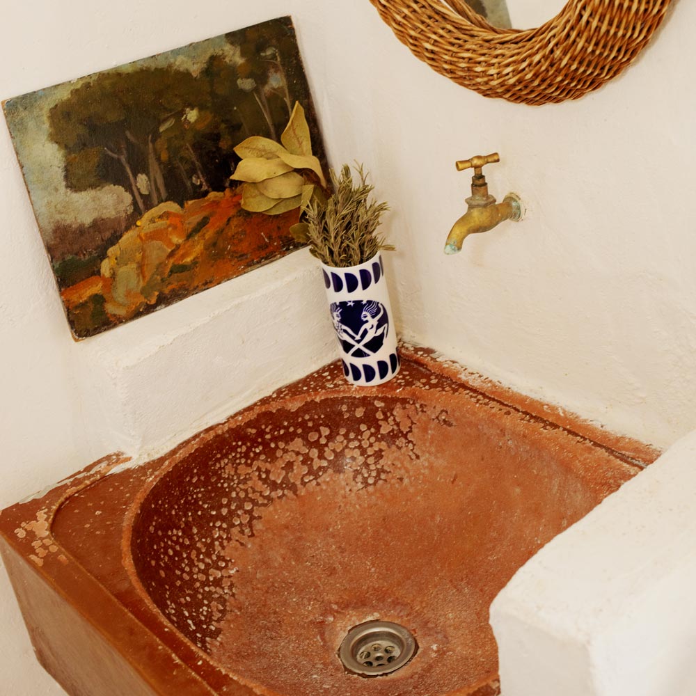 Ceramic sink with a vase and plant, wall art, and faucet in a bathroom setting.