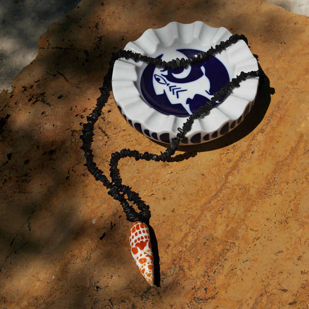 A white and navy porcelain valet tray set on a base and featuring a shell necklace.