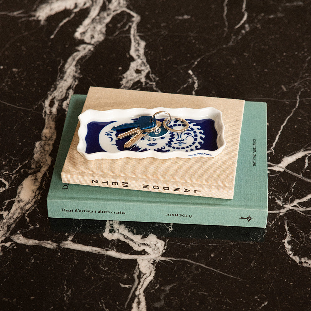 A porcelain tray decorated with images of stars on top of some books on a table, with a set of house keys on it.
