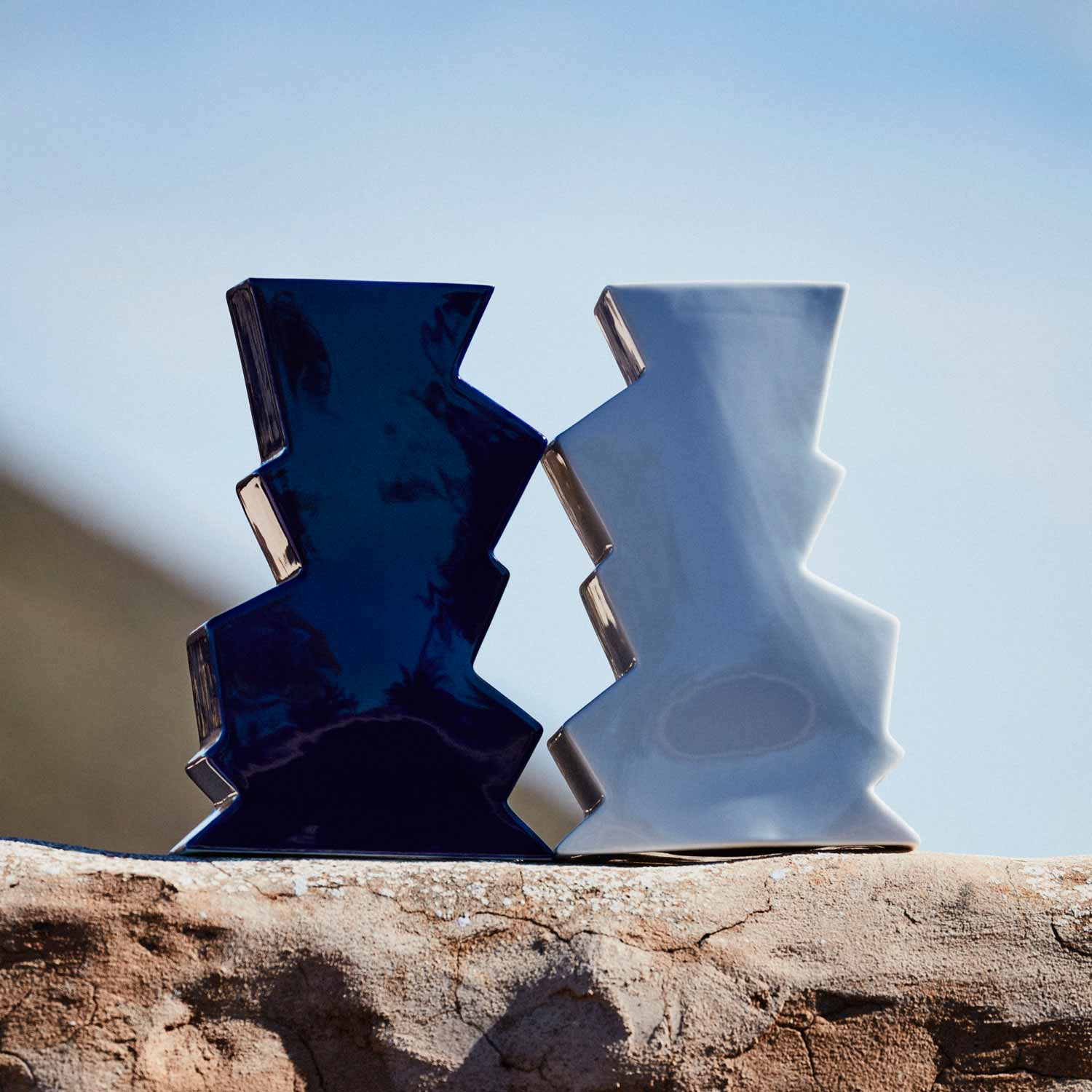 Two porcelain vases – one white and the other navy – on an outside wall.