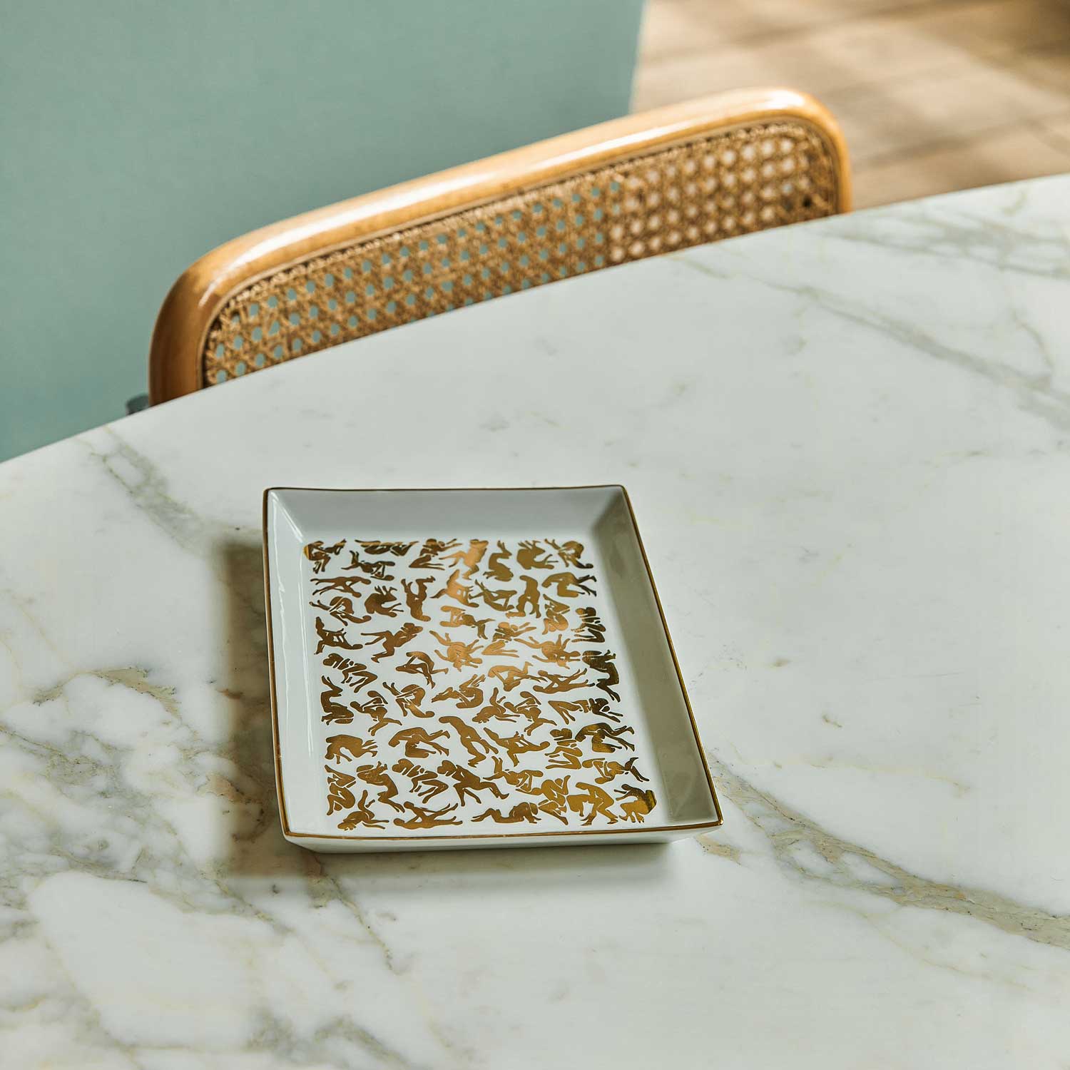 A white porcelain tray featuring a pattern of Kamasutra positions, displayed on a table.