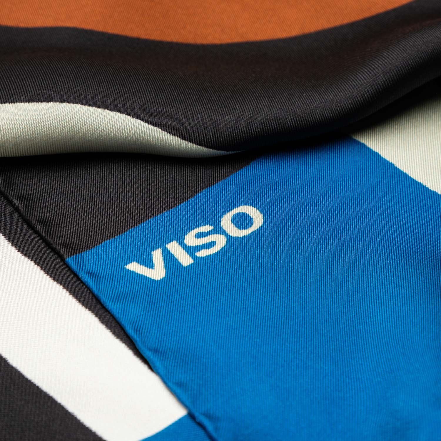 A detail of multicolored silk scarf with geometric patterns, featuring different colors such as black, red and blue, and the 'VISO' brand logo.