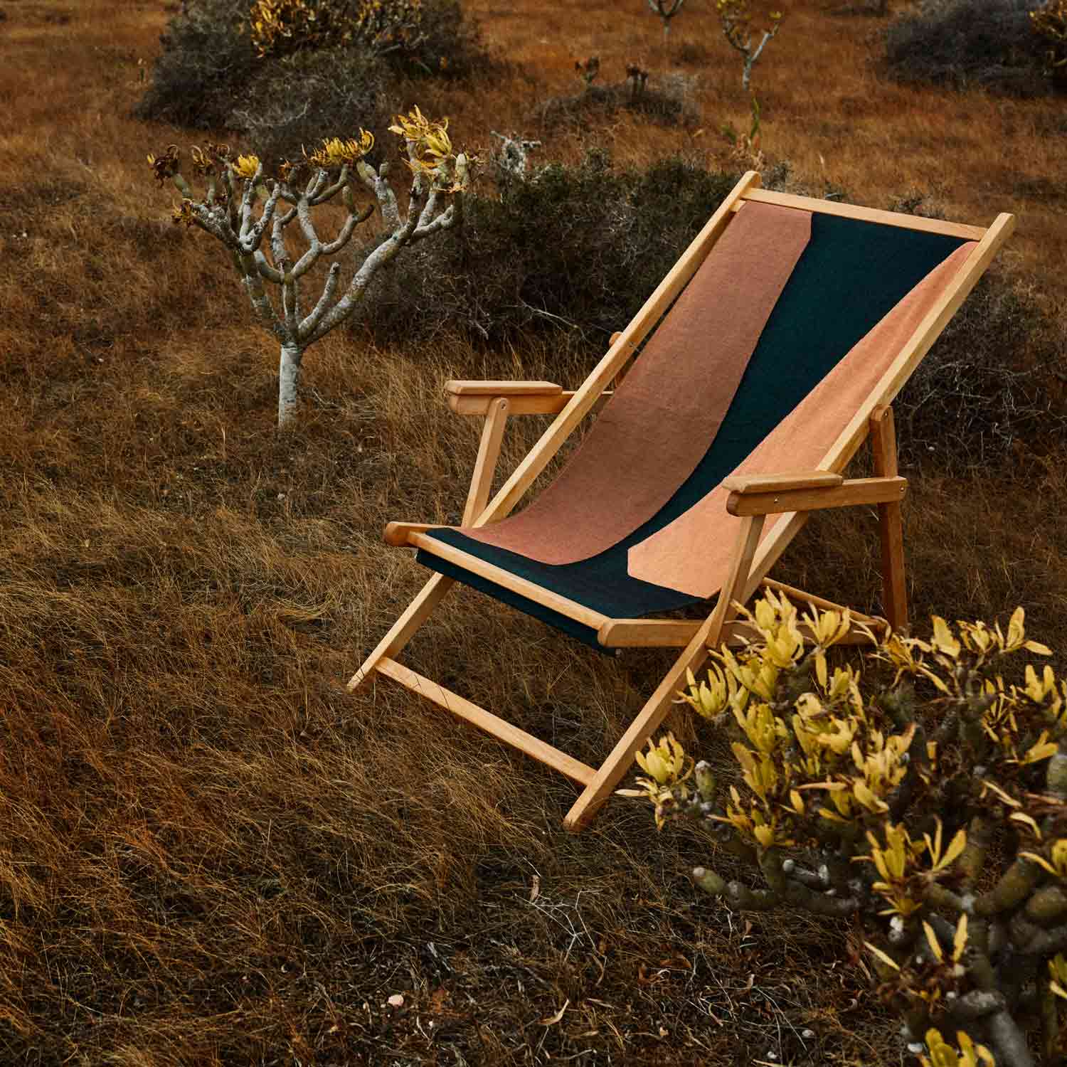 A folding beach chair with brown, orange, and black cotton tapestry backrest and seat, made of teak wood on a garden