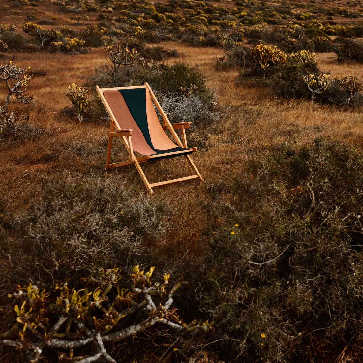 A folding beach chair with brown, orange, and black cotton tapestry backrest and seat, made of teak wood on a garden