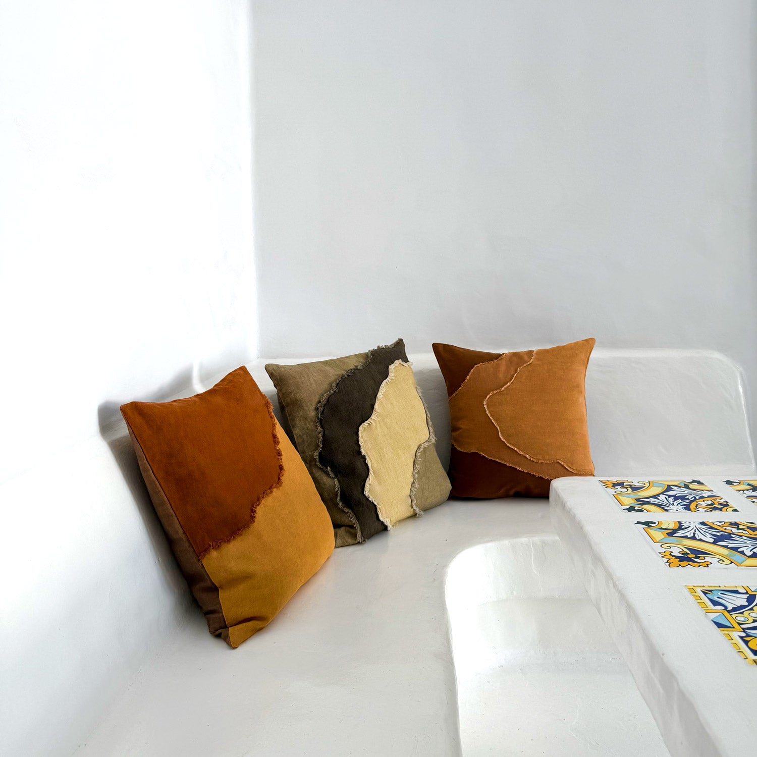 Three patterned pillows on a white sofa with a colorful blanket.