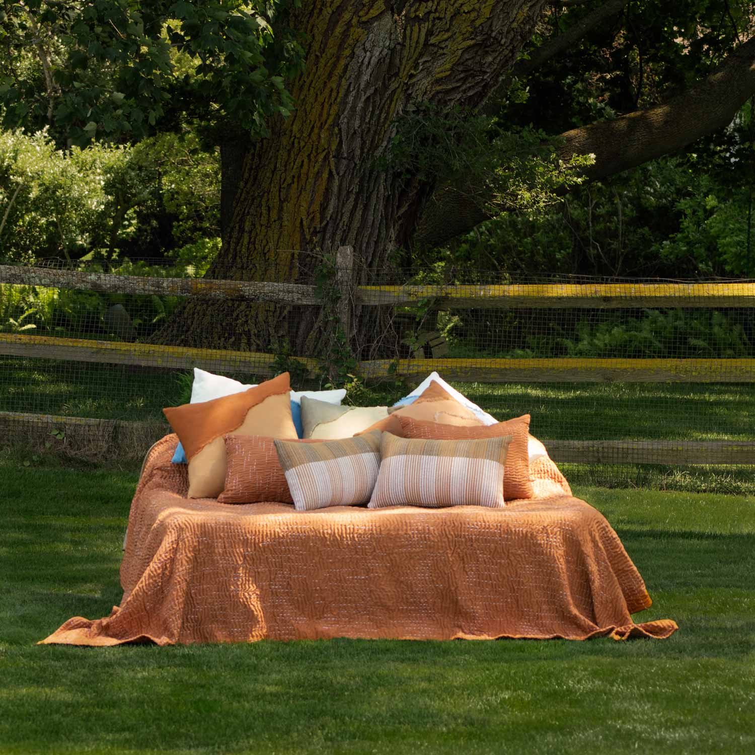 Outdoor setting with a bed covered in orange blanket and pillows on grass