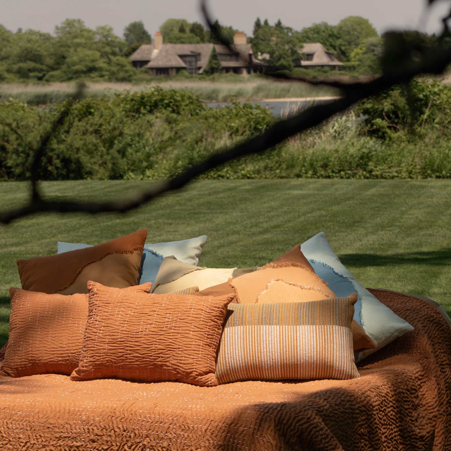 Collection of outdoor pillows on a sofa with a scenic background of trees and a house.
