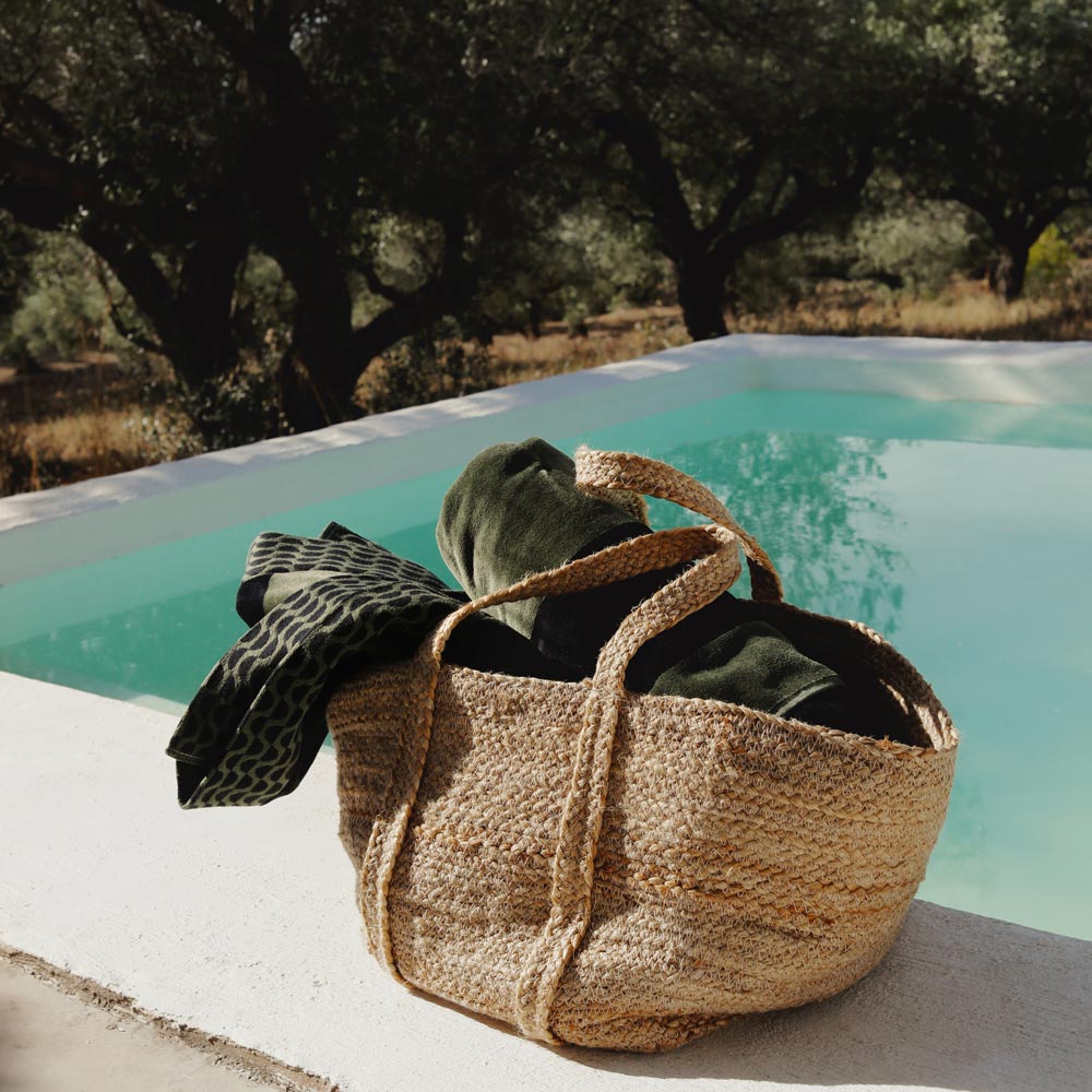Woven bag with green and black cotton  towel inside by a poolside