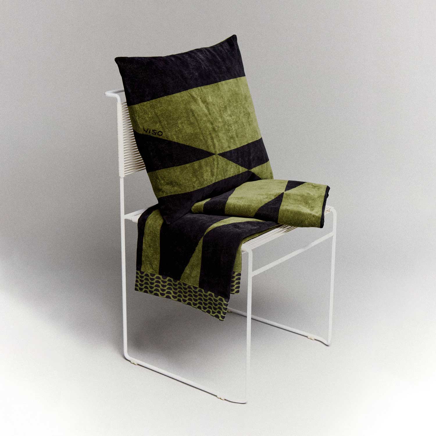 A green and black towel and cushion on a white chair.