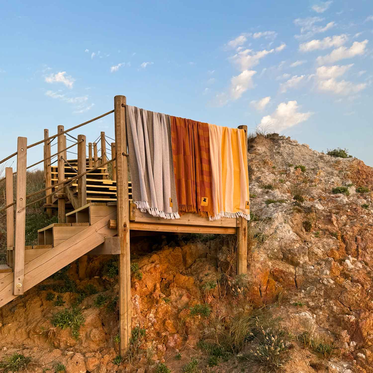 Striped towel draped over a wooden railing with a scenic background of a rocky hillside and blue sky.