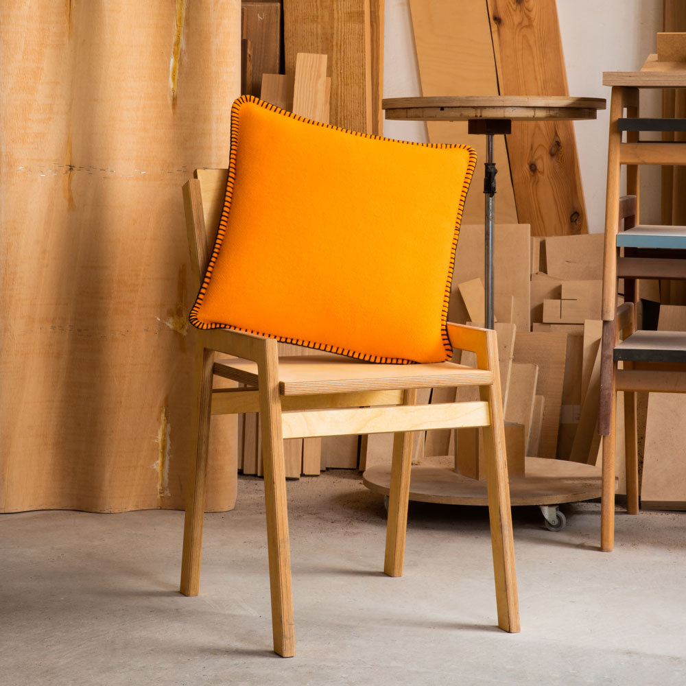An orange and black merino pillow on a chair in a studio.